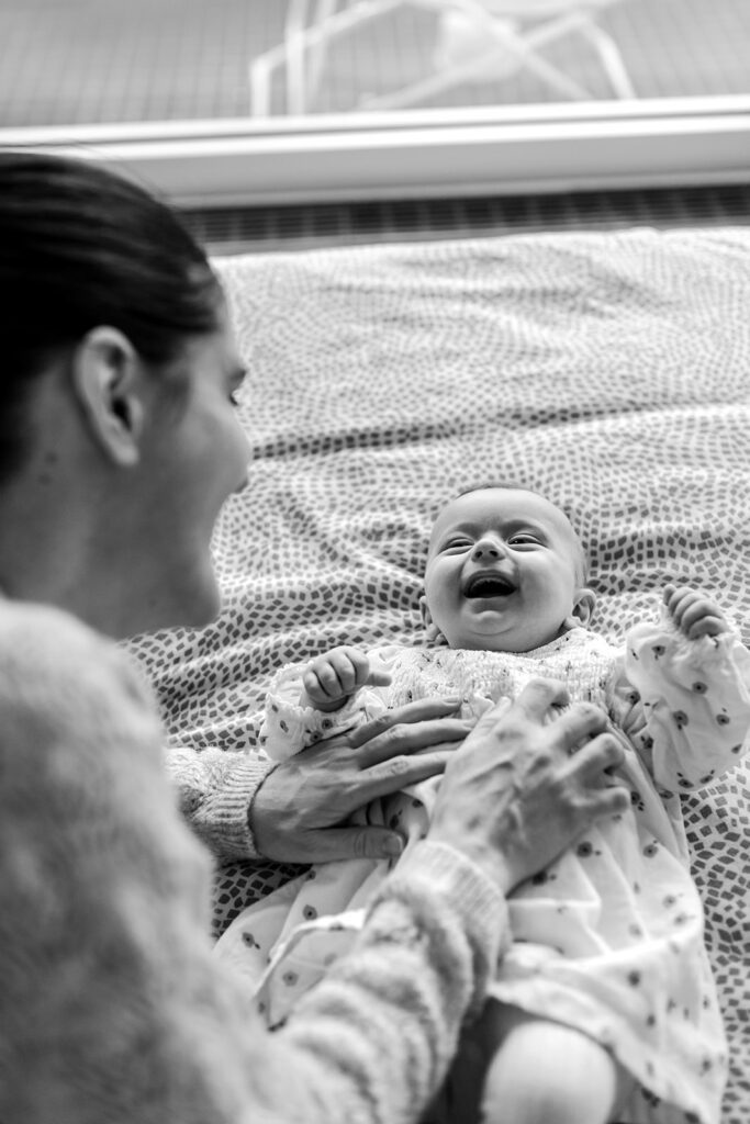 Mother playing with her laughing baby on the bed at home