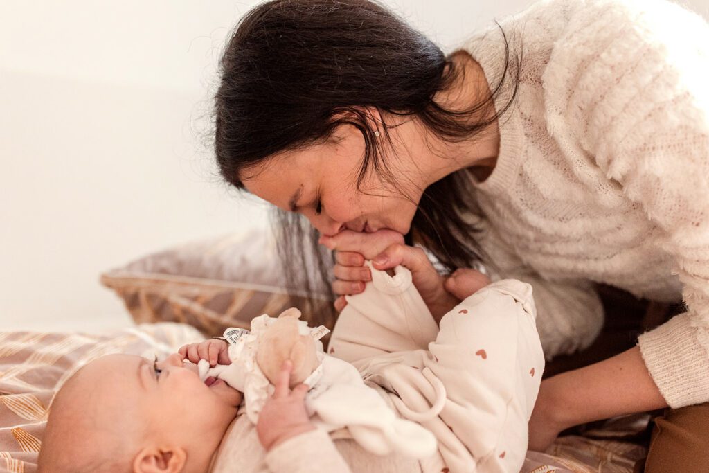 Mother kissing her baby's foot on the bed at home
