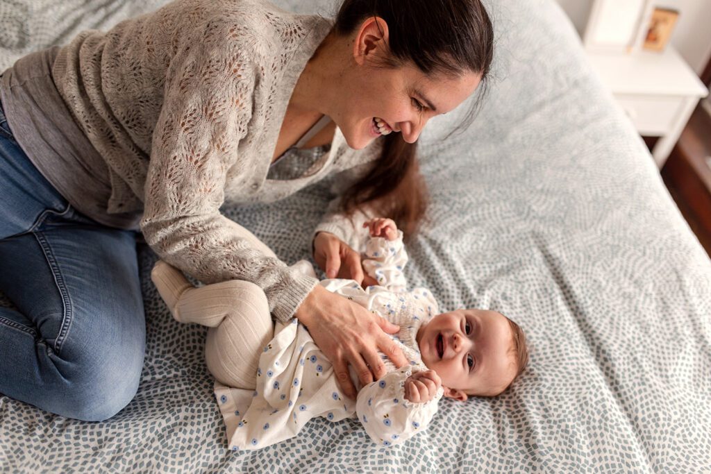 Mother playing with her smiling baby on the bed at home