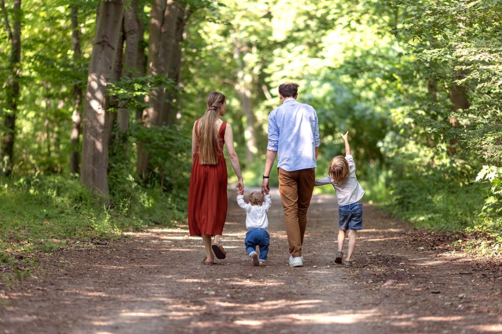 une famille marche en se tenant la main dans la forêt, de dos