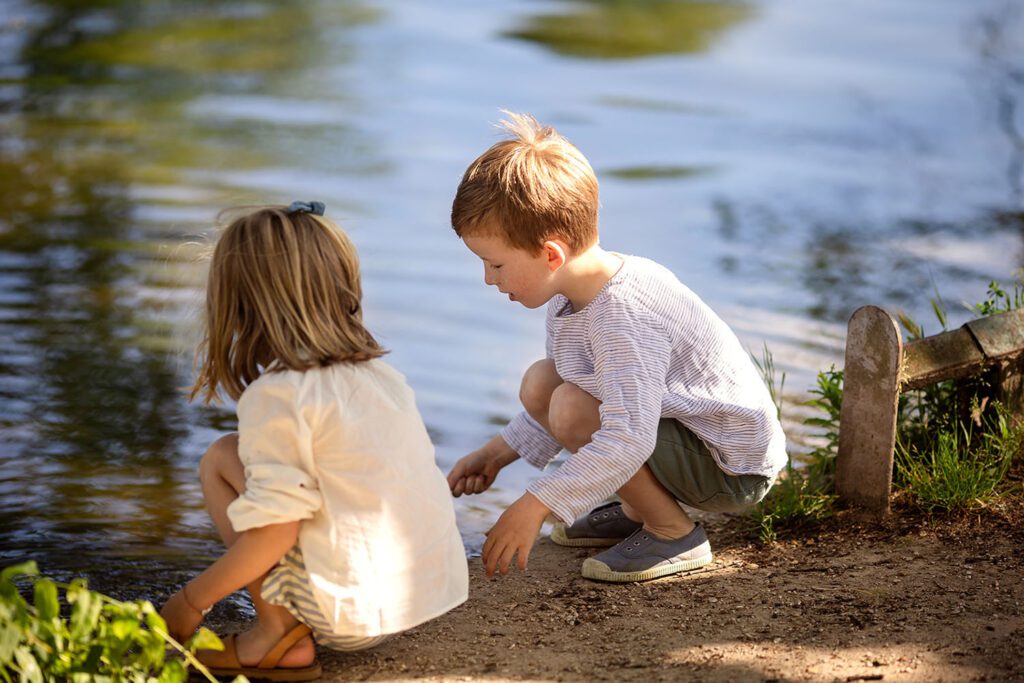 Two children playing together near a lake in a park