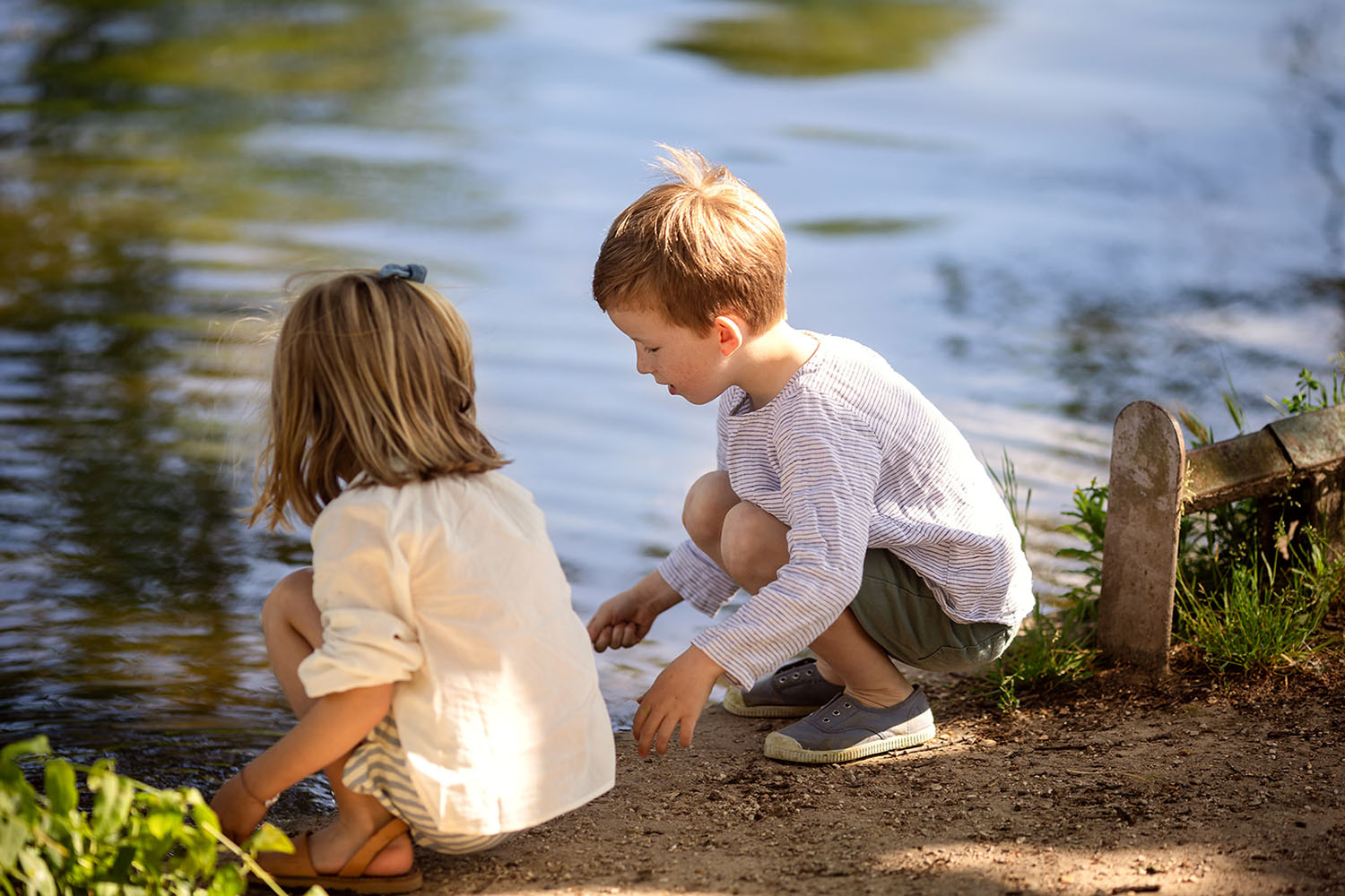 Two children playing together near a lake in a park