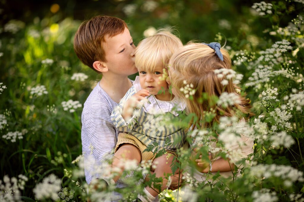 siblings are holding their baby brother, flowers surround them