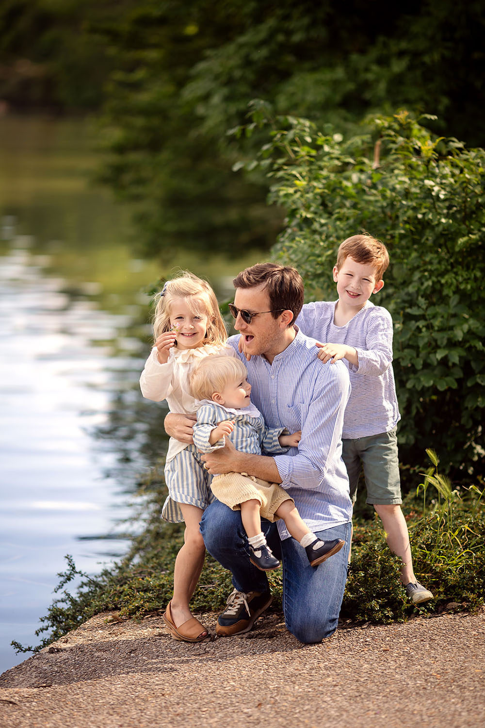 a father posing with his 3 kids near a lake during a photo session