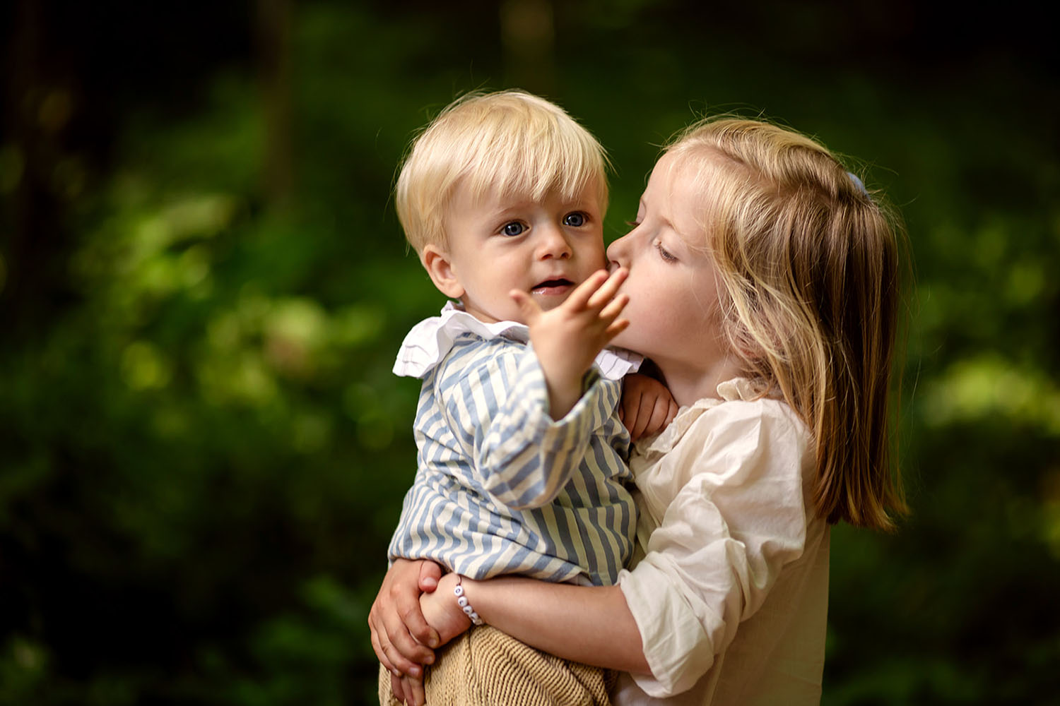 a little girl holds her baby brother in the park