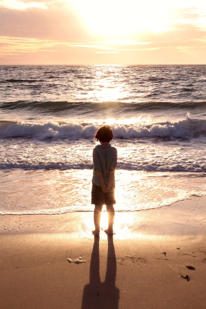 Child standing at the water's edge during sunset