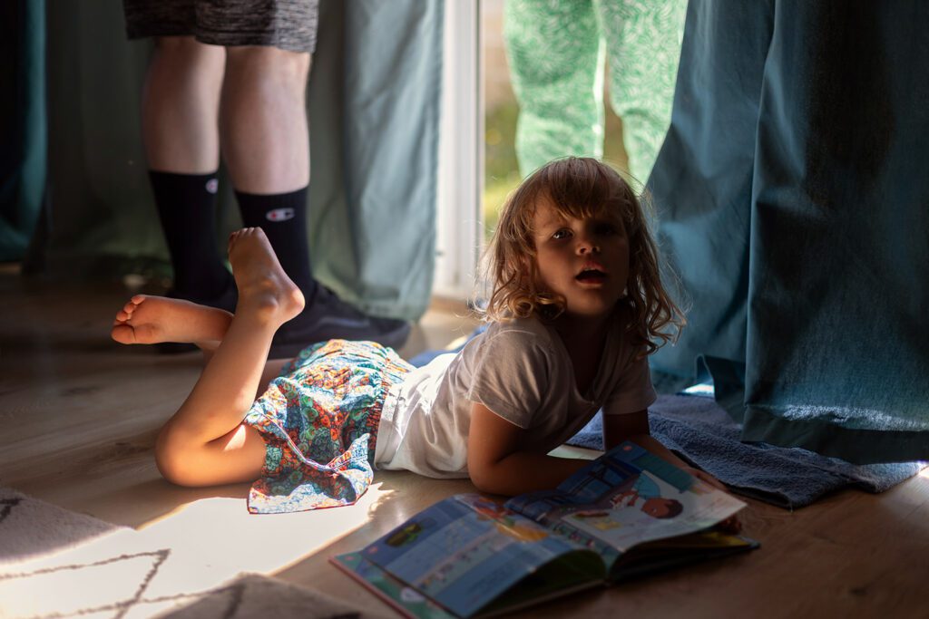 a little girl reading a book on the floor during a Day in the life session