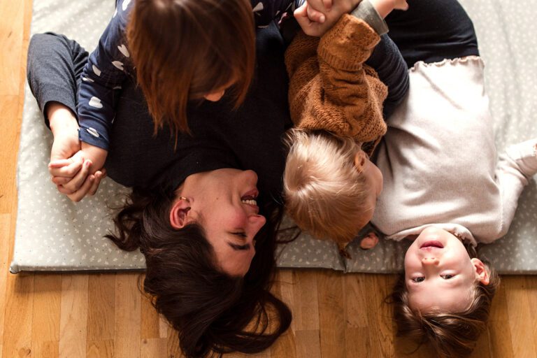 a mother with her 3 kids laughing on the living room floor