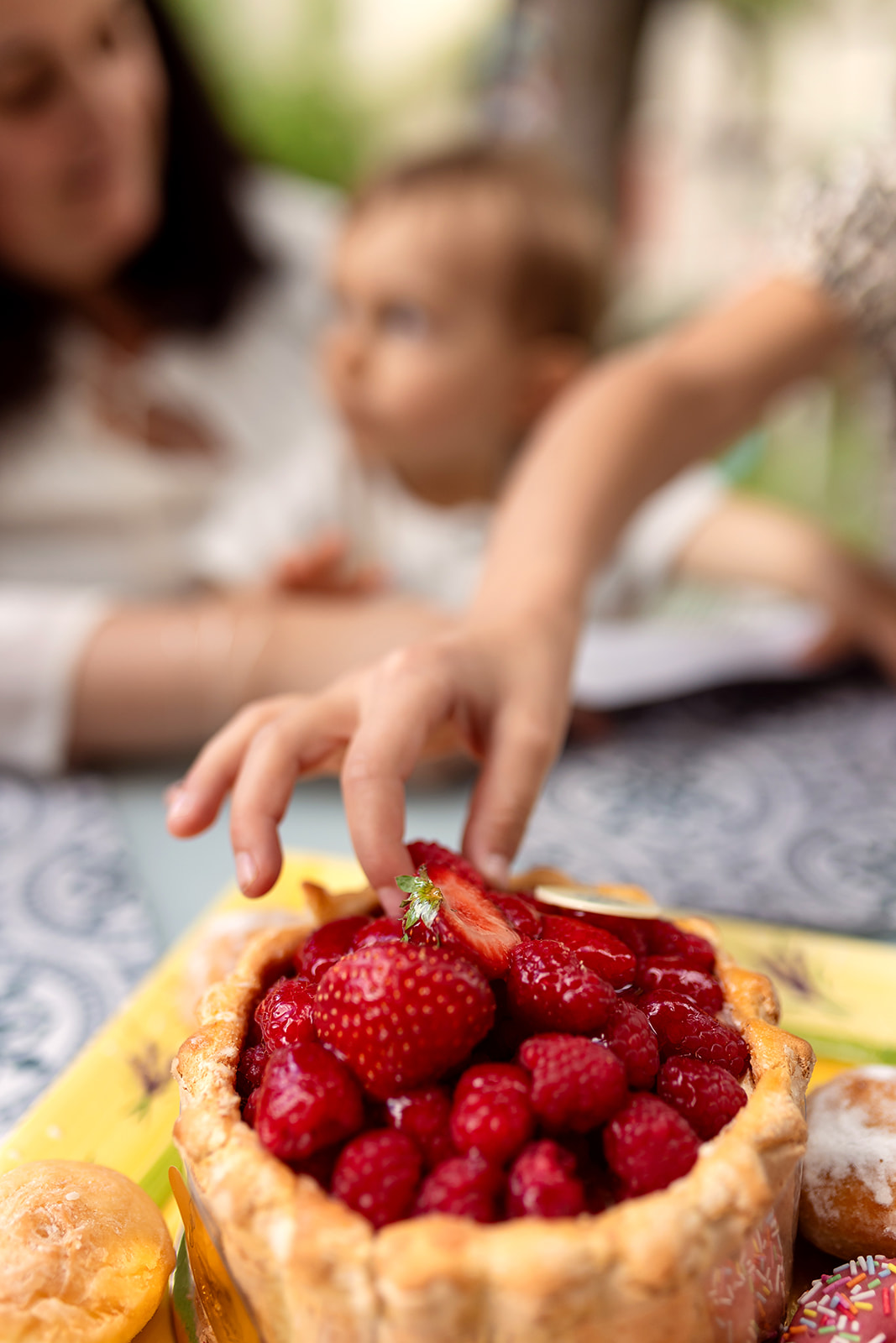 the small hand of a child sampling a strawberry on a cake