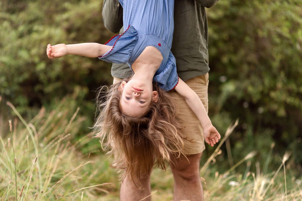 a dad holds his daughter upside down to play during a session with a family photographer Dublin
