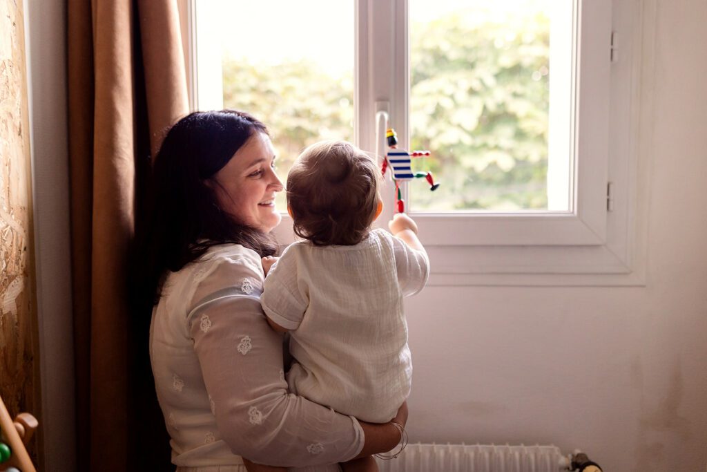 a mother holds her toddler and they look out the window