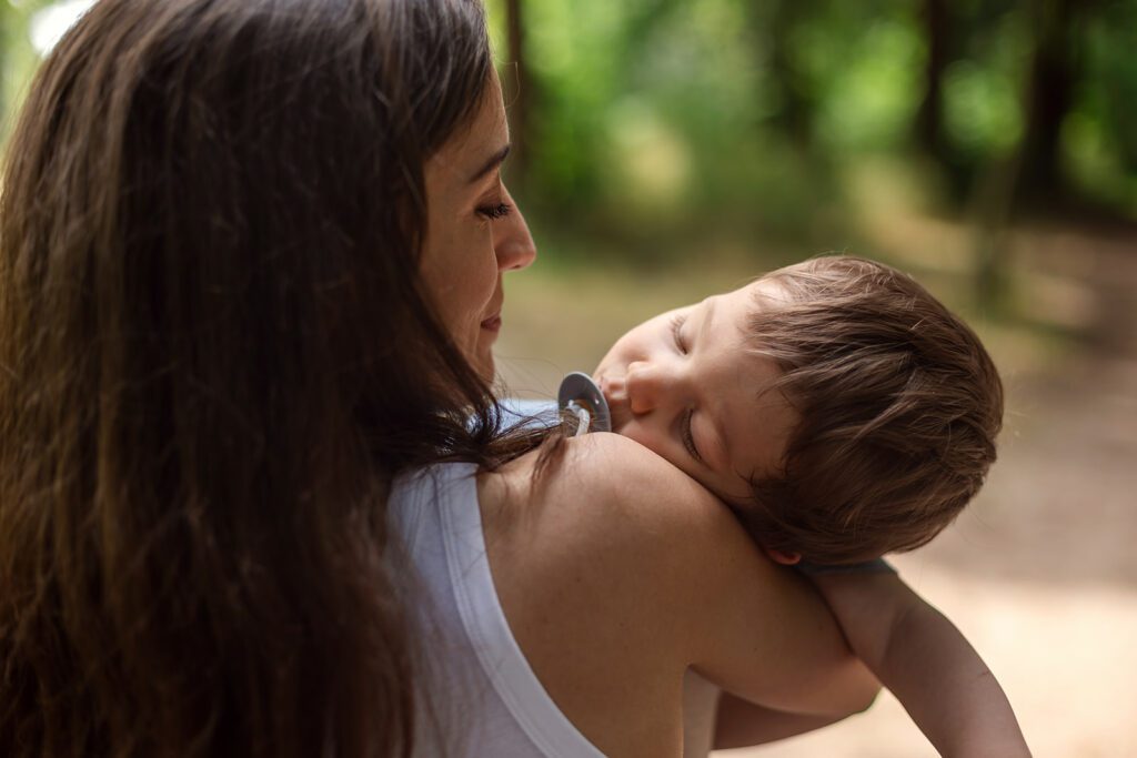 a mother holds her toddler who fell asleep after playing at the park