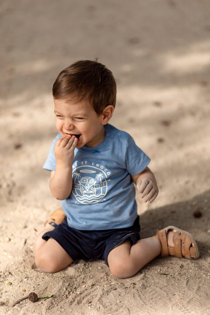 a toddler boy is sitting on the floor at the park, smiling