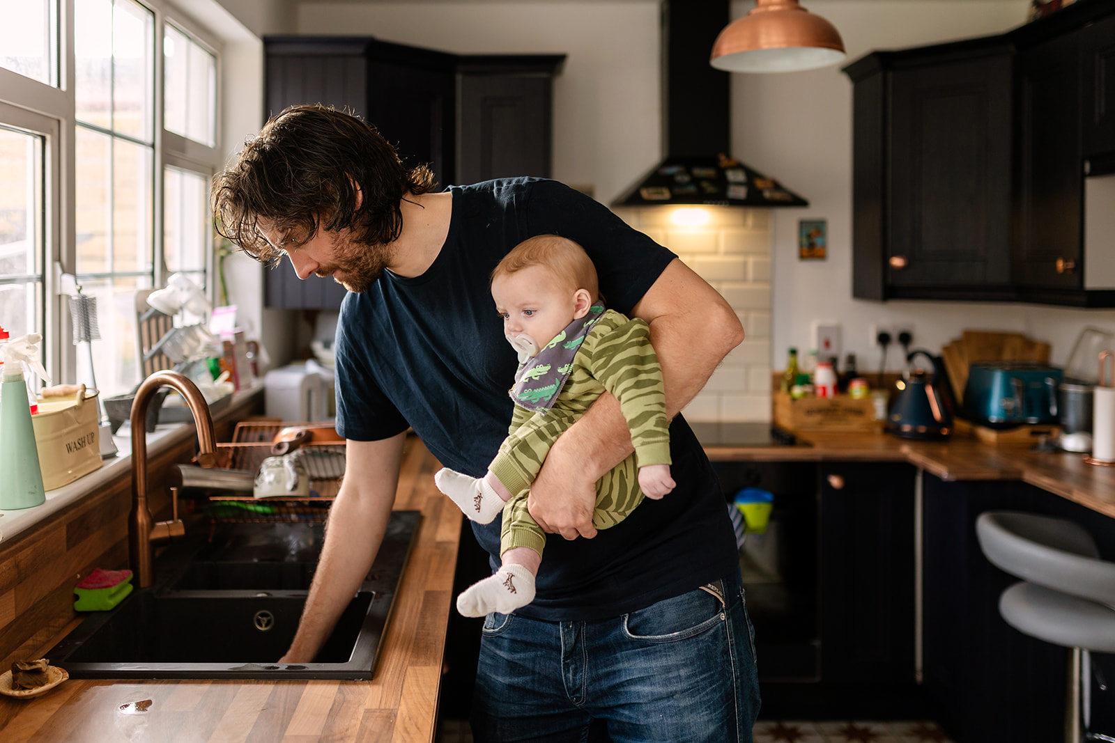 documentary family portraits of a father doing chores in the kitchen holding his baby