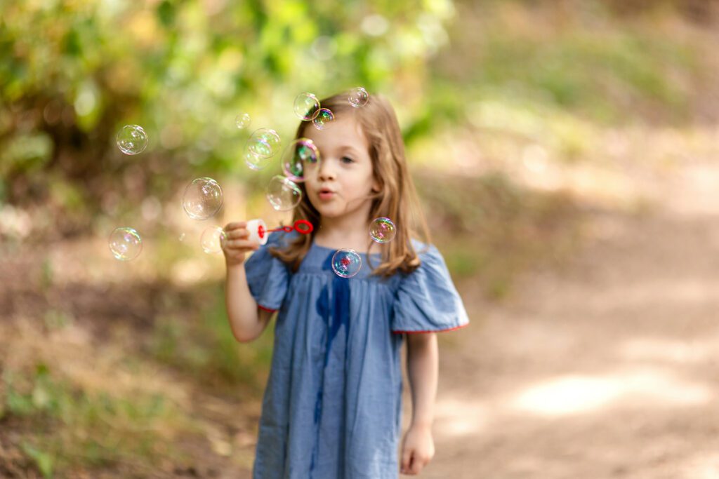 little girl blowing bubbles at the park