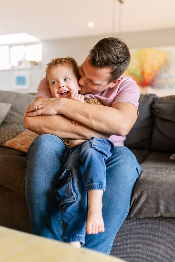 Father cuddling his young son on the sofa at home
