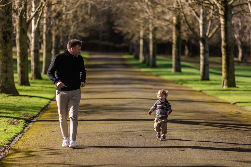 father and toddler son running around in memorial garden park