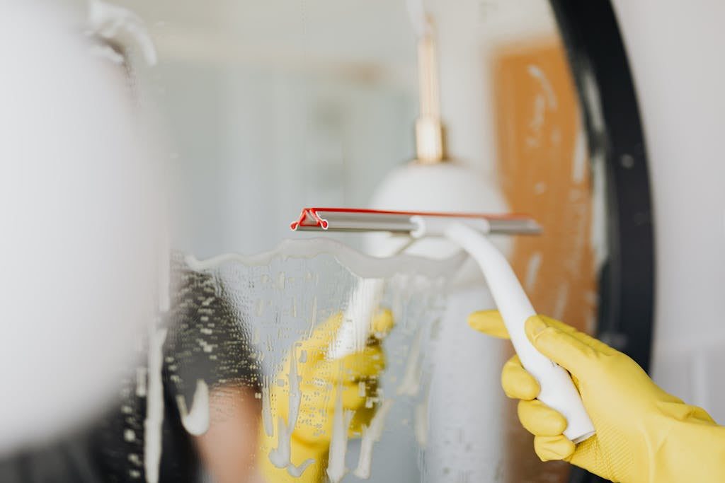 Person using a squeegee to clean a foamy bathroom mirror indoors. Gift ideas for parents of a newborn