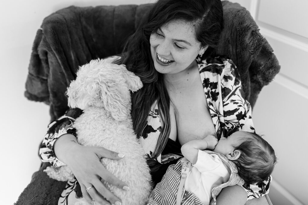 mother breastfeeding newborn and cuddling dog during an unposed newborn photography session