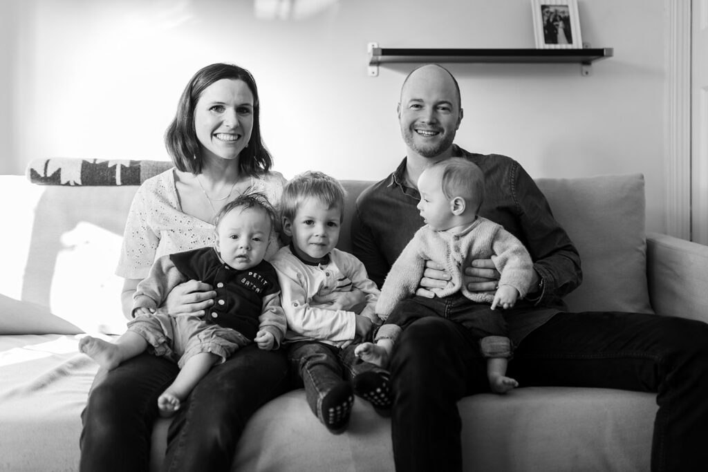 family with parents and 3 kids smiling and sitting on their sofa