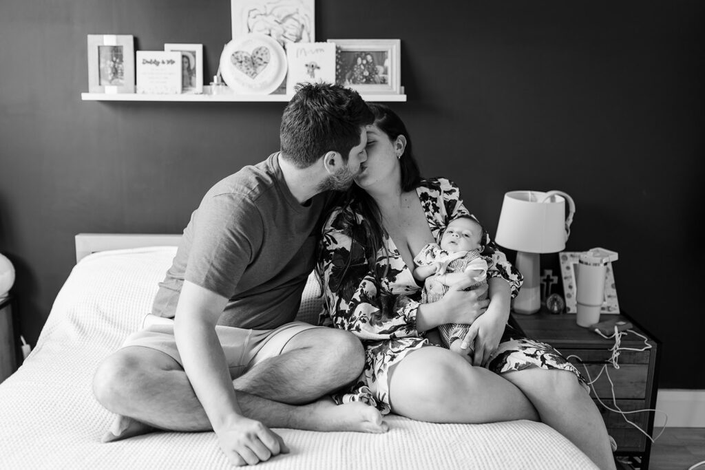 parents kissing while holding their newborn