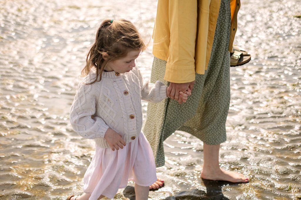 mum holding her daughter's hand and walking on the beach