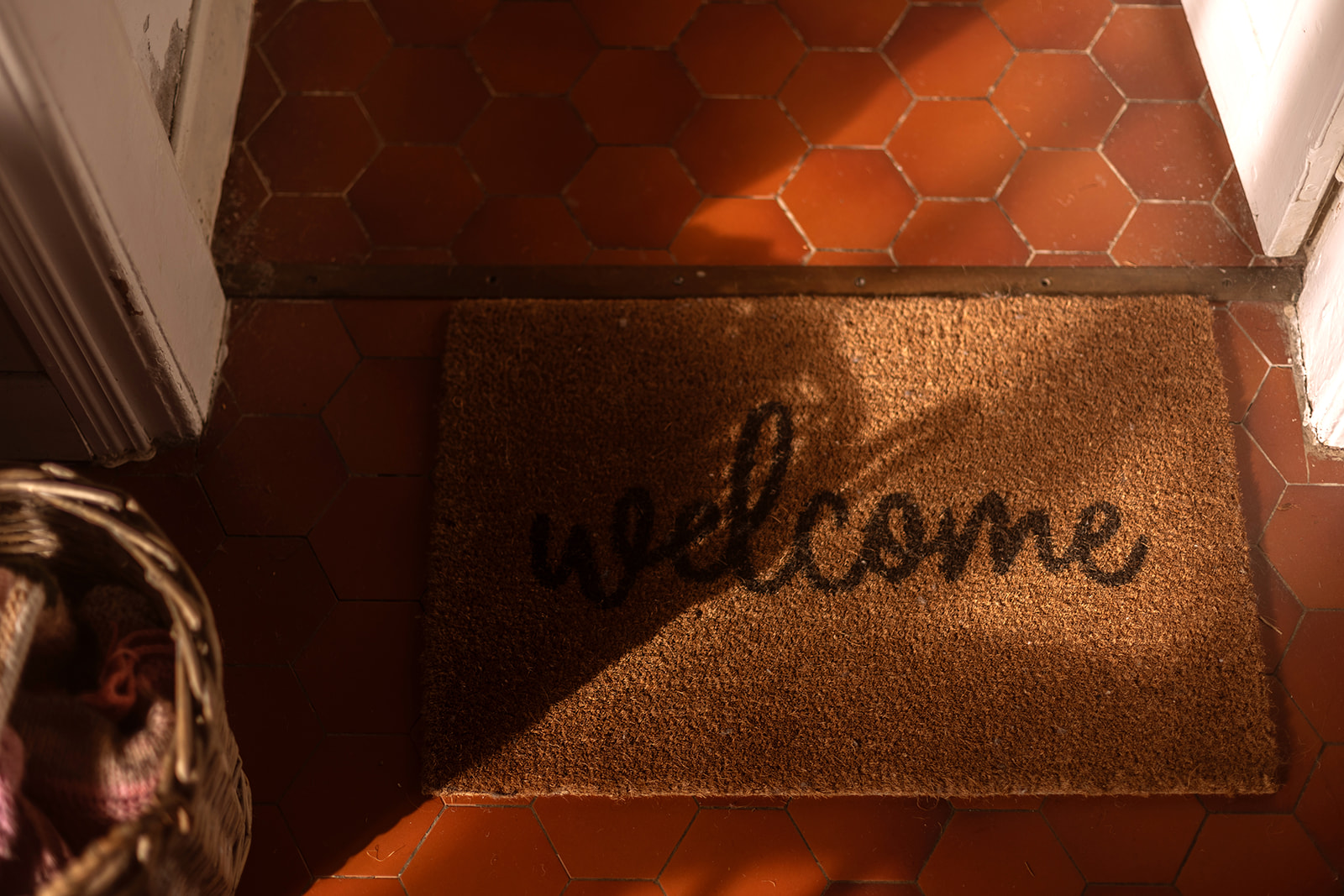 a doormat that says welcome and the sun casting shadows on the floor