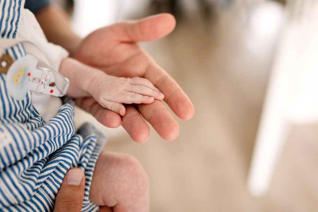 detail of a small baby's hand in his father's