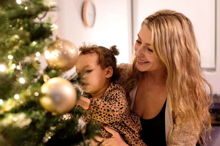 mom helping her toddler decorate the christmas tree