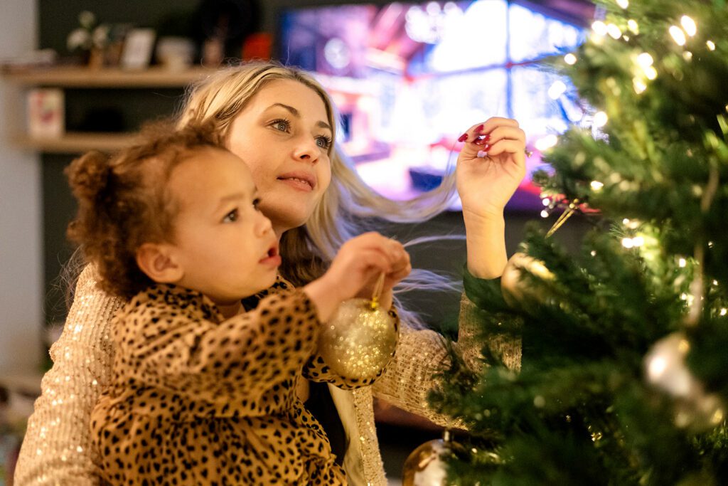 mom and daughter decorating the christmas tree for a christmas family photo session at home