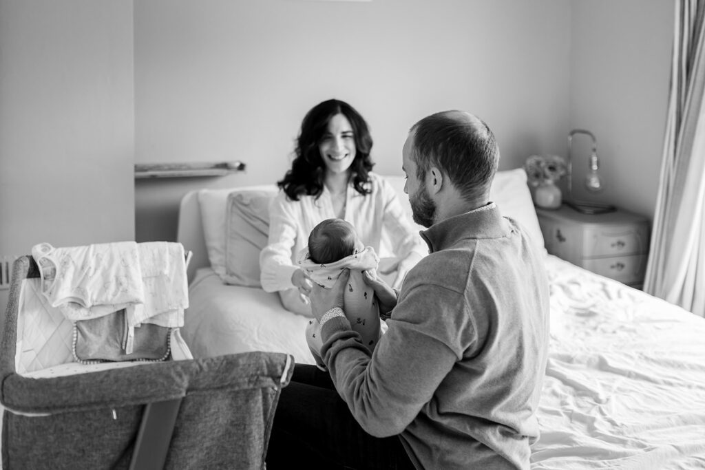 mother and father in their dublin home with their newborn baby, sitting on the family bed