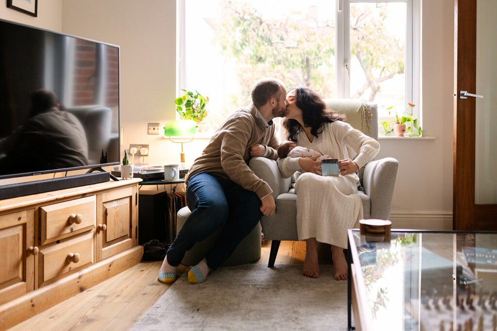 parents kissing while holding their newborn baby