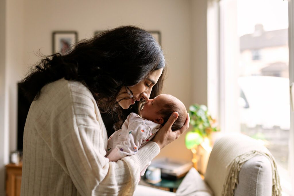mother kissing her newborn with beautiful window light at home