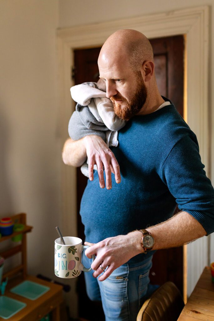 dad holding newborn in one hand and a cup of tea in the other