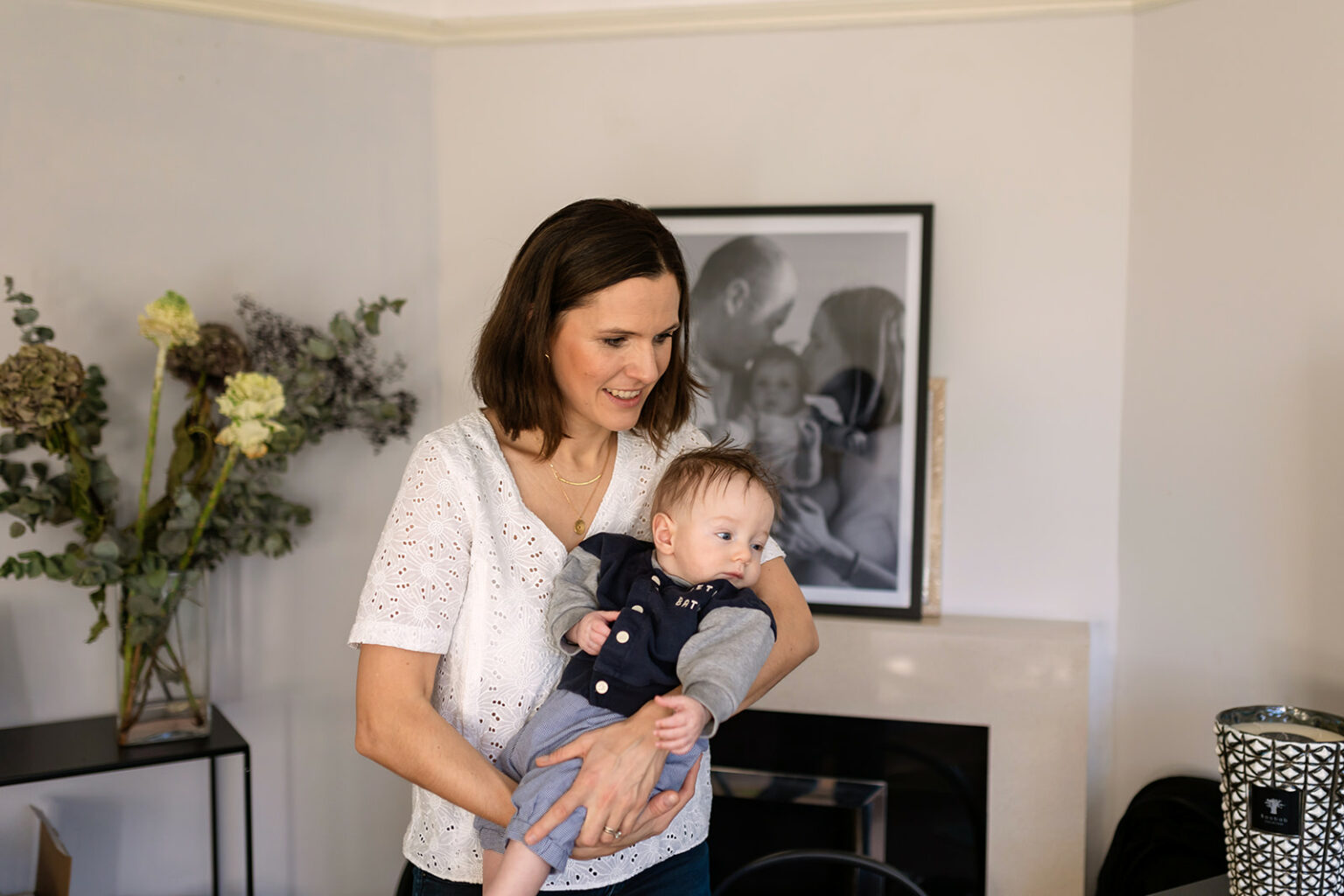Mother holding her baby beside a large framed family photograph in the living room